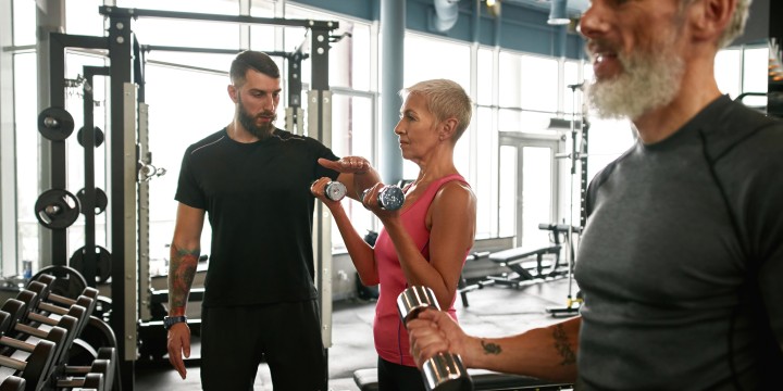 Trening siłowy na siłowni – grupa osób ćwiczących z hantlami pod okiem trenera